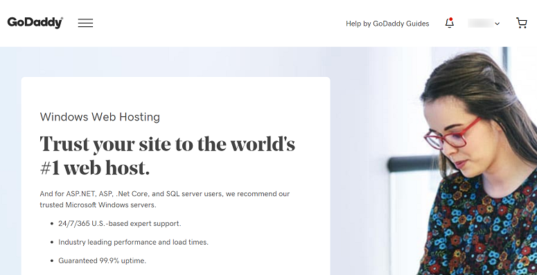 Woman in colorful top focuses on a laptop. GoDaddy site text: "Trust your site to the world's #1 web host." Professional setting.