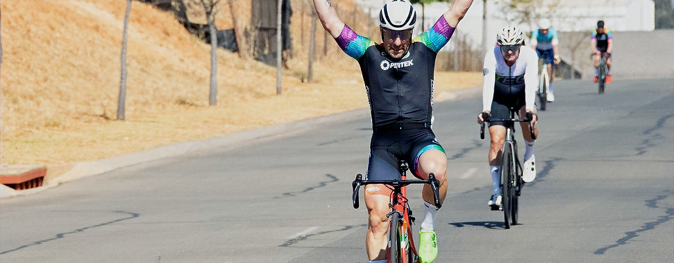 Cyclist celebrating victory in road race with arms raised, leading group.