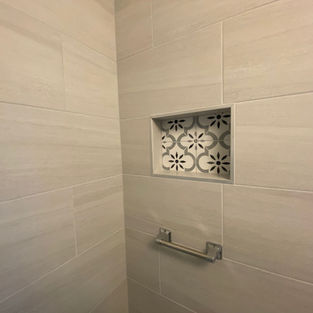 Built-in shower shelf with floral patterned accent tile in remodeled bathroom