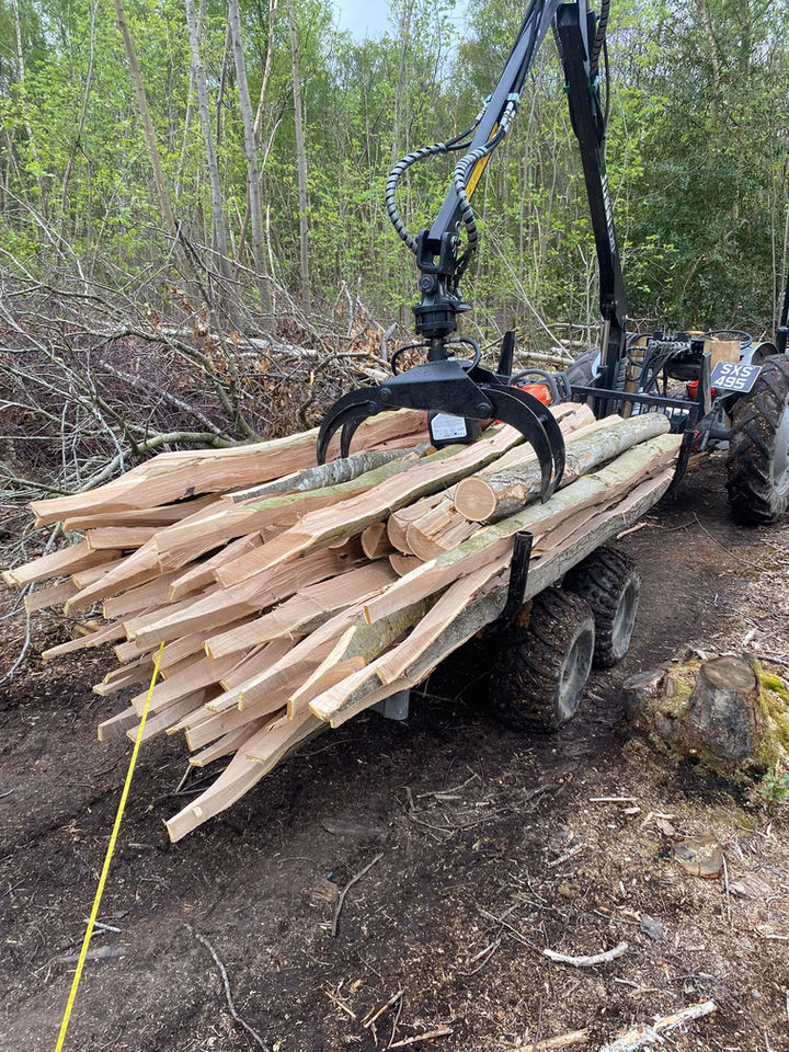 Machine loading timber into a trailer; tractor in a forest setting.