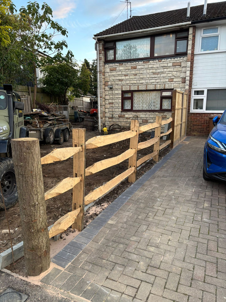 Wooden fence along a driveway, house visible in the background, new construction project.