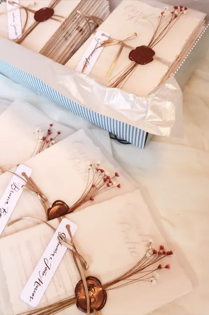 Convite de casamento elegante, feito em papel aquarela, luva em folha vegetal com laço de cetim e selo de cera do monograma do casal, além de sempre vivas nas cores da cerimônia. 