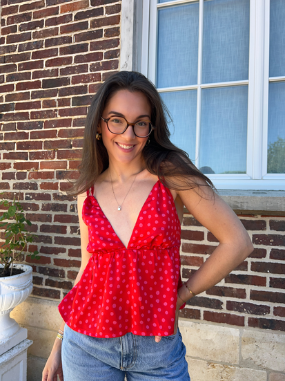 Femme brune portant un top cousu main dans un tissu rouge à pois rose.