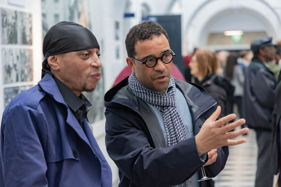 Two men conversing at an exhibition, one gesturing