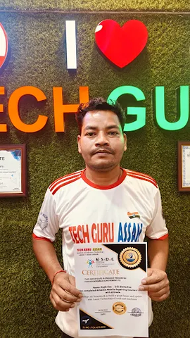 A male student from TechGuru Assam proudly holding an NSDC-approved certificate in front of a wall with "I ❤️ TECH GU" lettering.