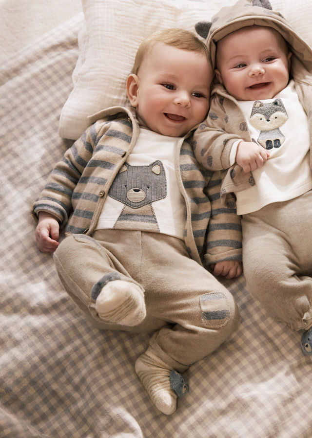 Zwei lächelnde Babys liegen nebeneinander in passender Kleidung auf Decke.