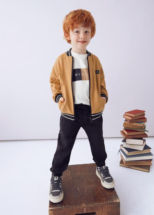 Kleiner Junge mit rotem Haar, brauner Jacke, stehend auf Holzkiste.