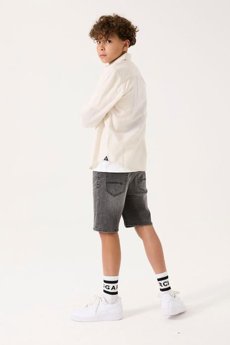 Junger Junge mit gekreuzten Armen, weißem Langarmshirt und grauen Shorts.