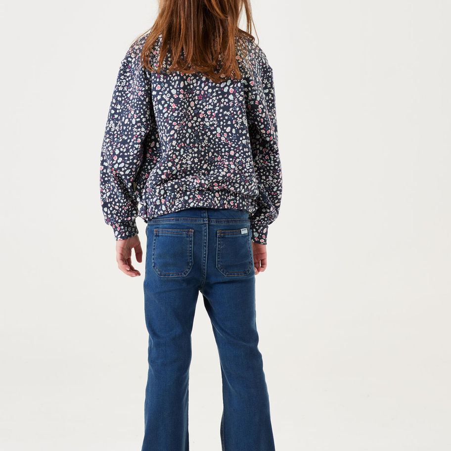 Mädchen von hinten in gemustertem Oberteil und blauer Jeans.