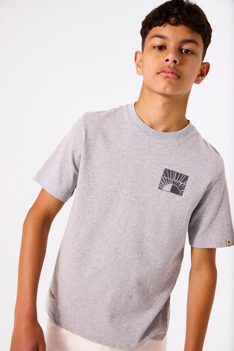 Junger Junge trägt hellgraues T-Shirt mit abstraktem Berggrafik auf der Brust.
