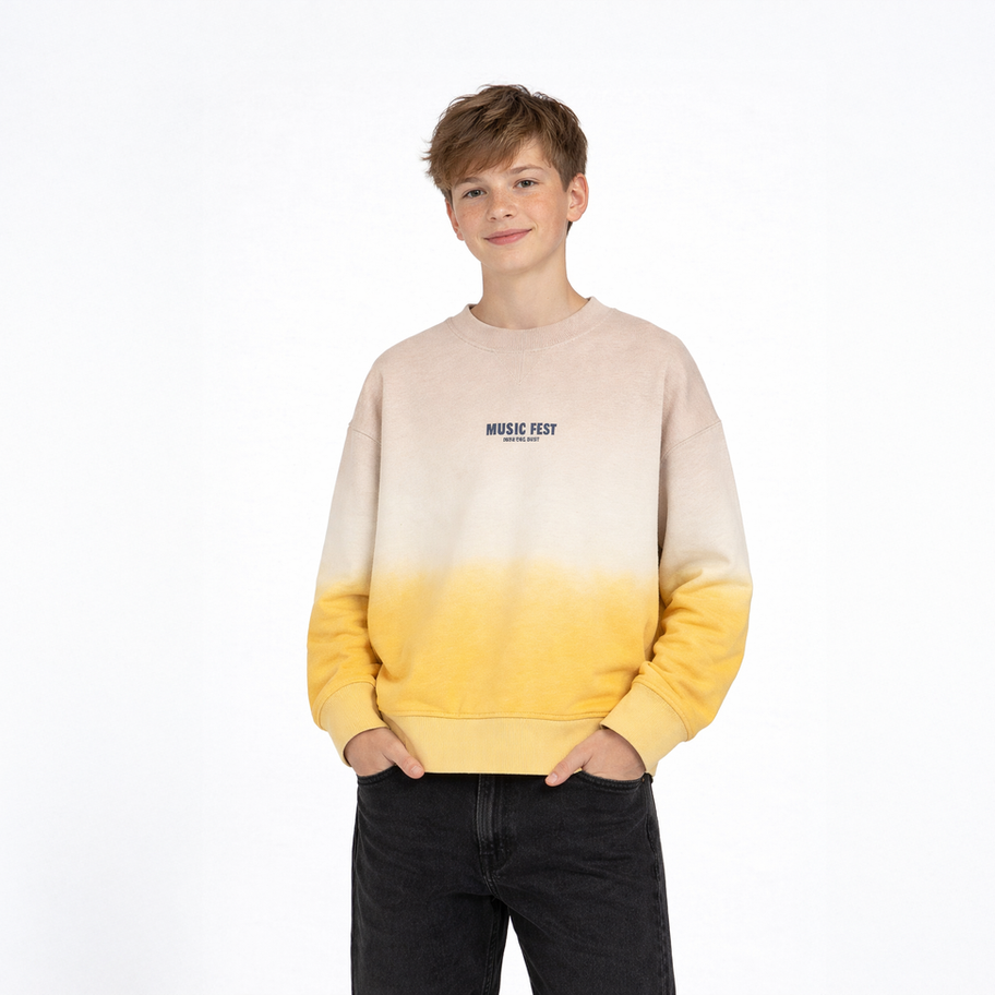 Junger Junge trägt beiges, gelbes Project X Paris Sweatshirt, Hände in Taschen.