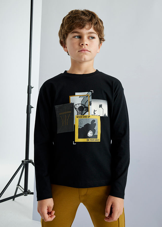 Junge trägt schwarzes Langarmshirt mit grafischem Druck und braune Hose.