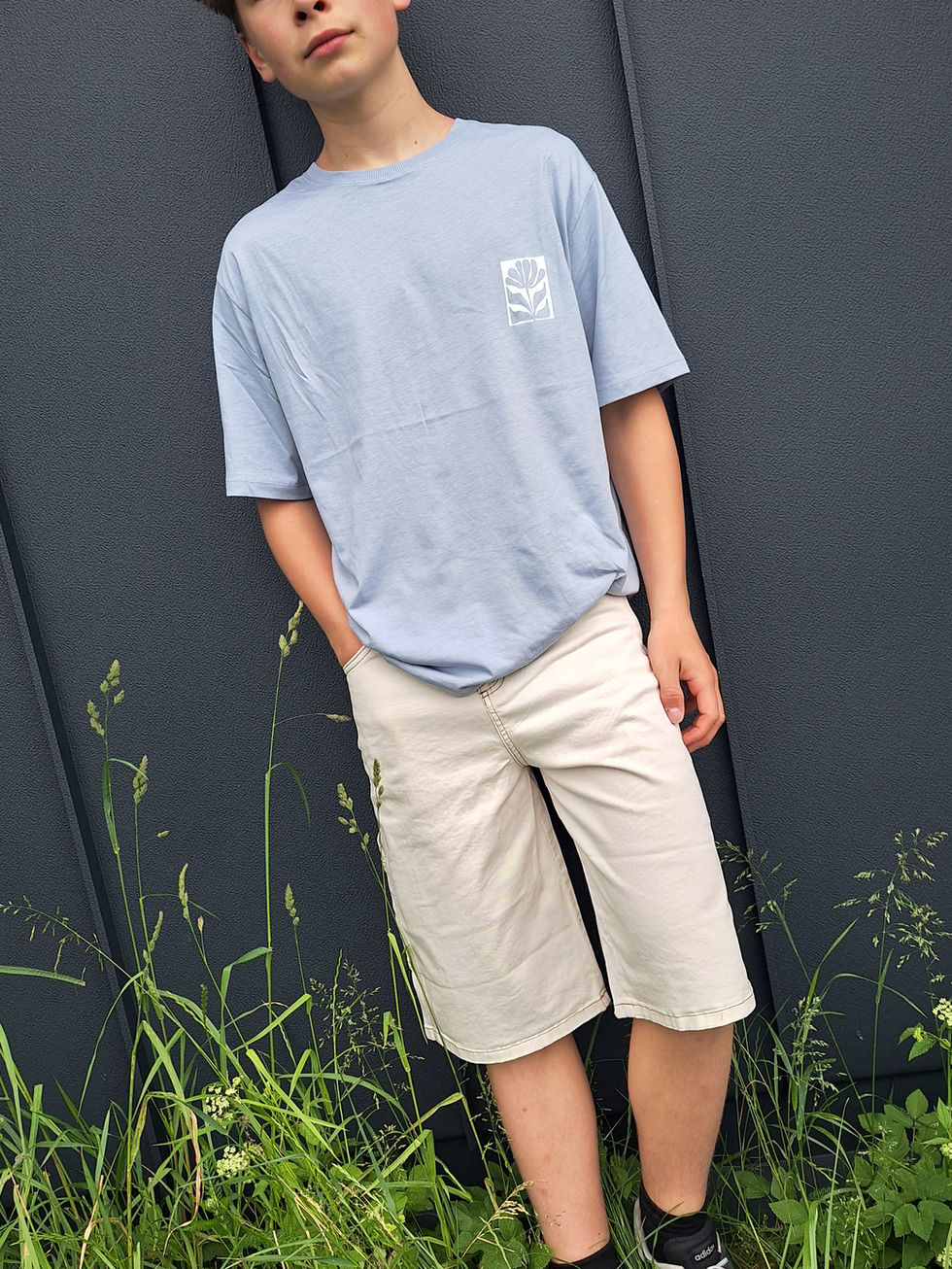 Person trägt hellblaues T-Shirt und beige Shorts vor dunkler Wand.