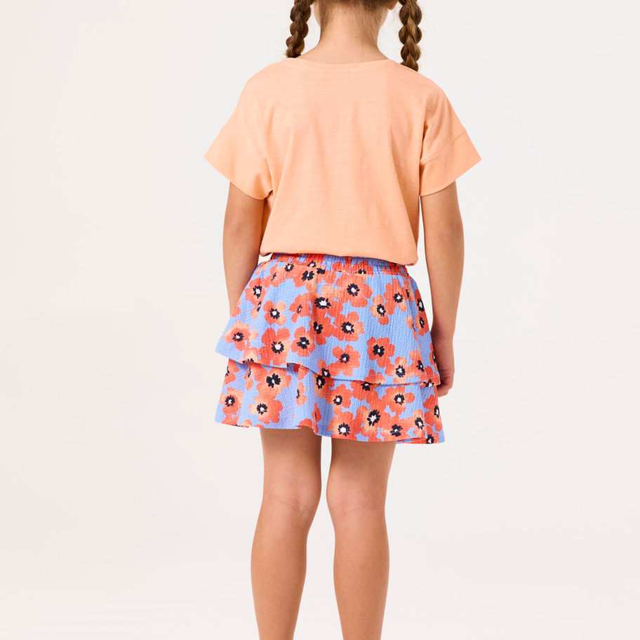 Kleines Mädchen von hinten, pfirsichfarbenes T-Shirt, geblümte Shorts, Zöpfe, helle Sandalen.