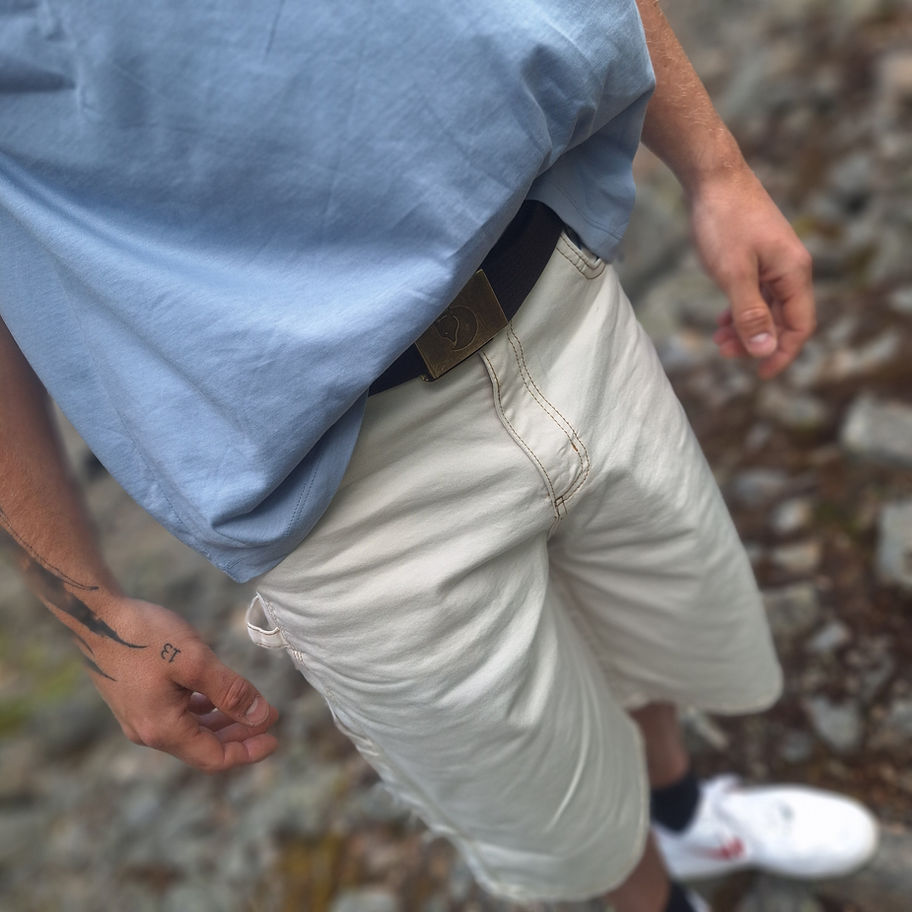 Person trägt hellblaues Hemd und beigefarbene Shorts draußen stehend.