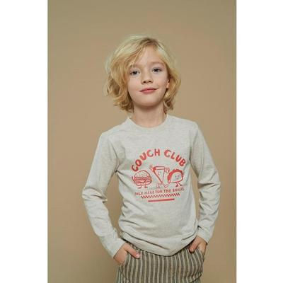 Junger Junge trägt beiges 'SUMMER CAMP' Langarmshirt mit gestreifter Hose.