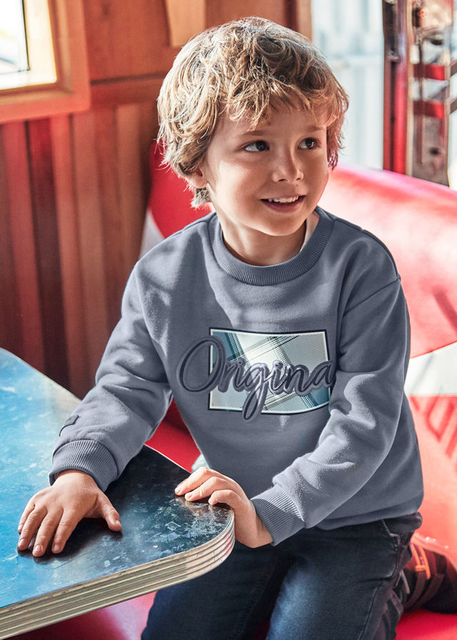 Kleiner Junge mit Locken trägt graues "Original" Shirt am Tisch.