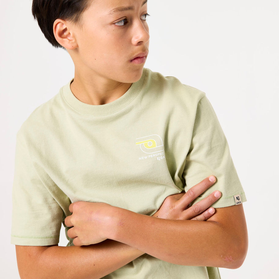 Junge trägt hellgrünes T-Shirt, Arme verschränkt, blickt nach rechts.