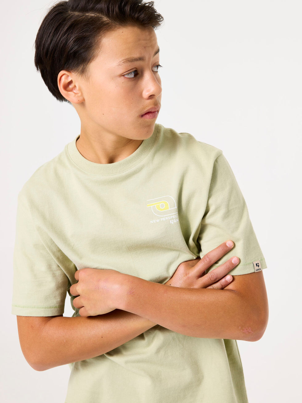 Junge trägt hellgrünes T-Shirt, Arme verschränkt, blickt nach rechts.