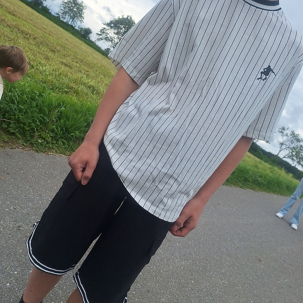 Junge Person in gestreiftem T-Shirt und Shorts auf Asphaltweg draußen.