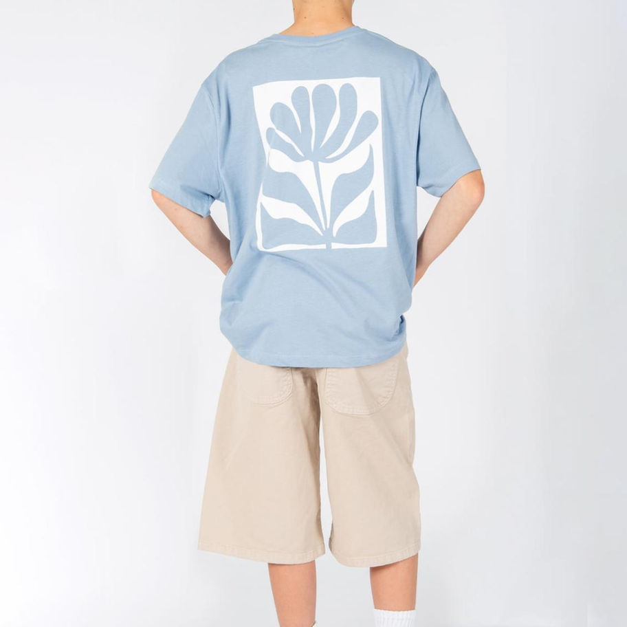 Person von hinten in blauem T-Shirt mit weißer Blumengrafik, beigen Shorts.