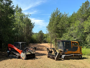 Two American Excavation compact track loaders equipped with heavy-duty forestry mulching attachments parked on a freshly cleared, evenly mulched path through a wooded area in Middle Tennessee.