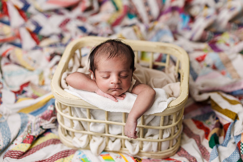 newborn baby boy posed in cream crate on vintage quilt for professional portrait 