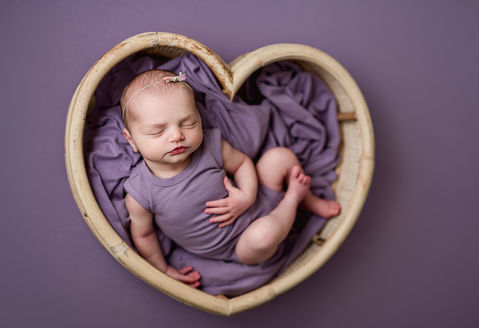 newborn baby girl in heart shaped prop, monochromatic purple newborn session portrait 