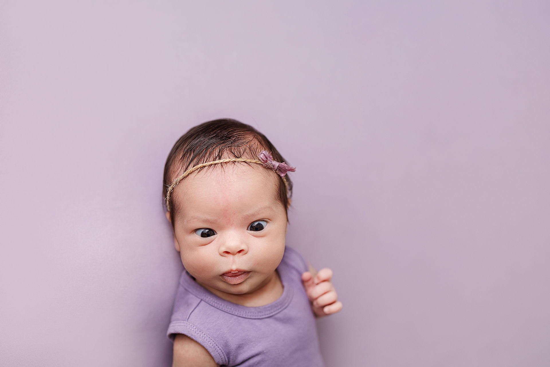 newborn baby girl in purple outfit on purple background professional newborn photo, newborn baby girl cross eyed picture