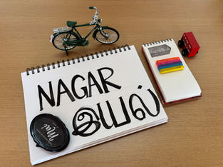 An a4 sheet with the word Nagariyal handpainted, along with a toy cycle and bus