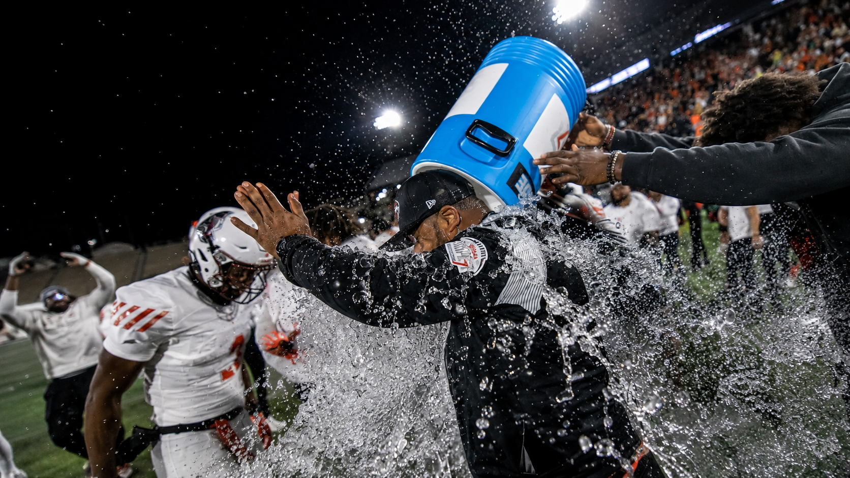Players celebrate a coach with a water-cooler shower under stadium lights