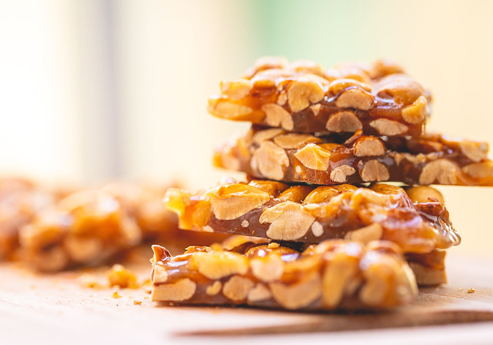 Stack of homemade peanut brittle pieces on a wooden board.