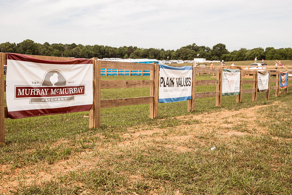 Sponsor banners, including Murray McMurray Hatchery and Plain Values, displayed along a fence at The Homestead Festival in Columbia, TN.