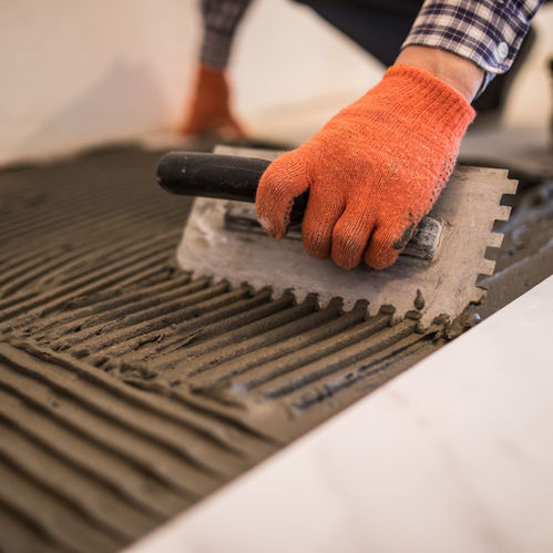 laying-ceramic-tiles-troweling-mortar-onto-concrete-floor-preparation-laying-white-floor-t