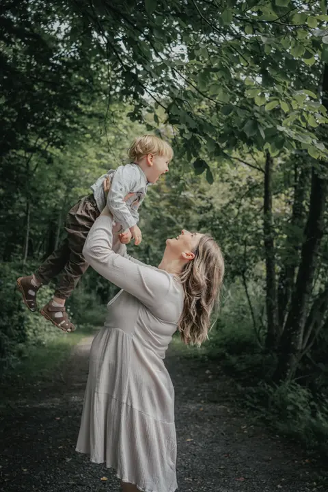 Familie mit schwangere Mutter, Partner und Kind umarmen sich liebevoll im Wald
