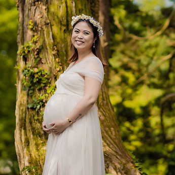 Smiling mother-to-be, hands on her bump, beneath the tall trees