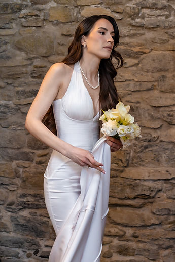 Albina, bouquet of calla lilies in hand, in front of the stone wall