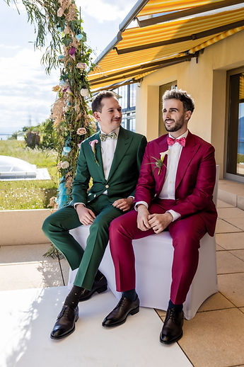 The grooms, seated, smile during the ceremony