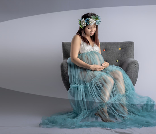 Future maman assise dans un fauteuil, en robe de tulle, au studio