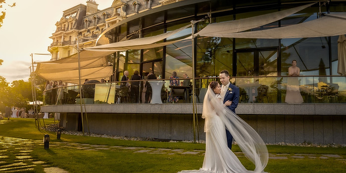 Bride with a long veil in the groom's arms, in front of a terrace at dusk