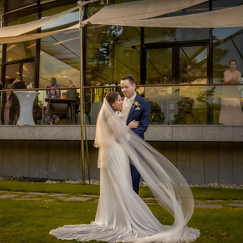 The bride's veil lifting in the wind, on a lawn at dusk
