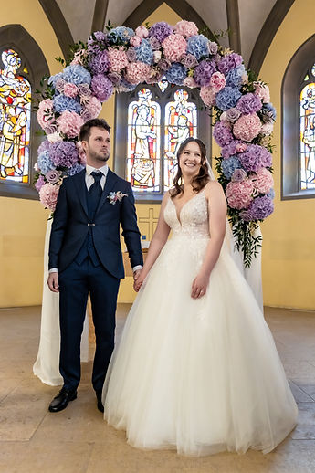 The couple hand in hand beneath the flower arch