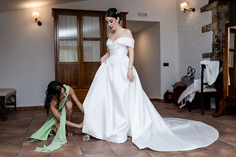 Gemma in her gown, a friend kneeling to adjust the hem