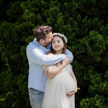 The father-to-be embraces the mother-to-be in front of a hedge