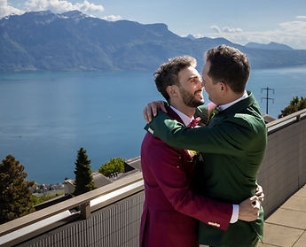 The grooms embrace, laughing, the lake behind them