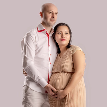 The father-to-be holds the mother-to-be, hands on her bump, in the studio
