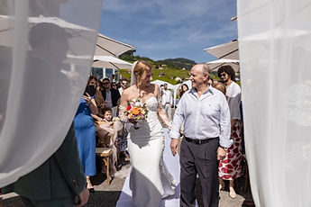Vahide walks towards the ceremony on a loved one's arm, between white drapes