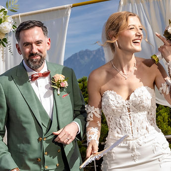 Vahide bursts out laughing beside Adrien under the floral arch, outdoor ceremony in Grandvaux, Lavaux