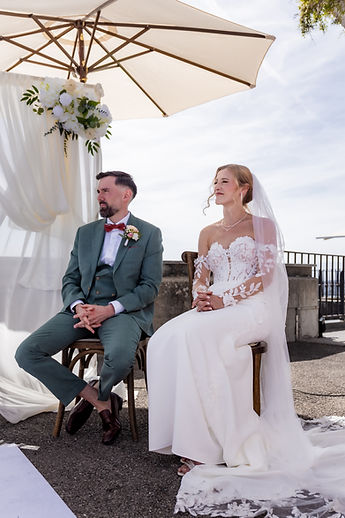 The couple seated beneath the parasols, in front of the flower arch