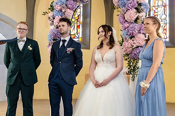 The couple with two loved ones in front of the flower arch